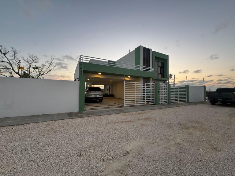 Modern green and white shipping container home with garage, car parked inside, gravel driveway at dusk