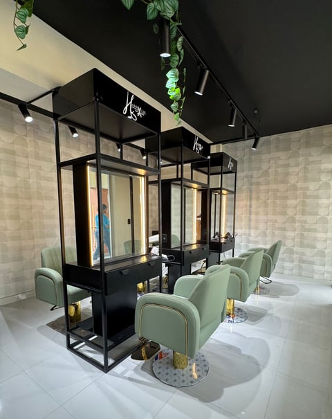 Modern salon interior with black framed workstations, mint green chairs, white tile walls, and hanging plants overhead
