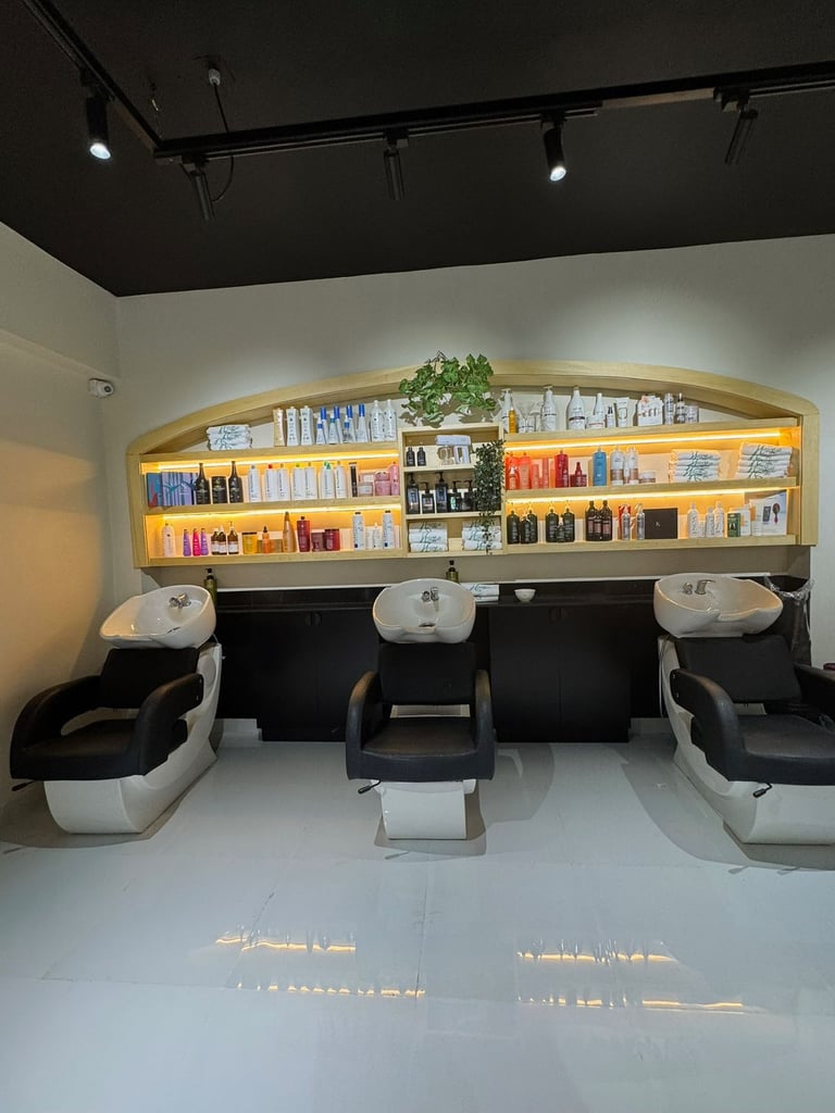 Modern salon interior with three black and white wash stations positioned under illuminated shelving displaying beauty products
