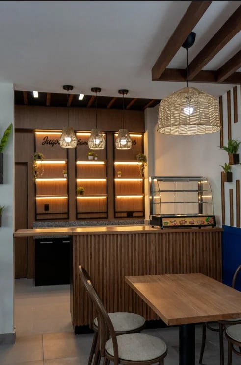 Modern bakery or cafe interior with illuminated display cabinets, wooden beams, pendant lighting, and dining table in foreground