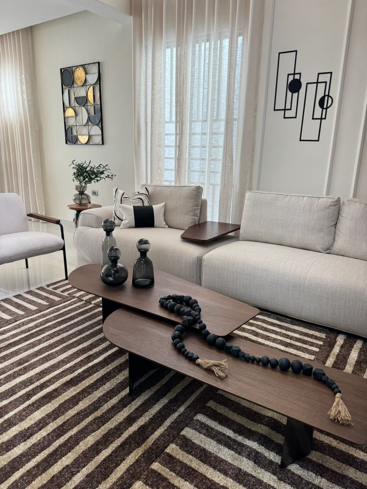 Modern minimalist living room with beige sofa, striped rug, dark wood coffee table, and contemporary wall art
