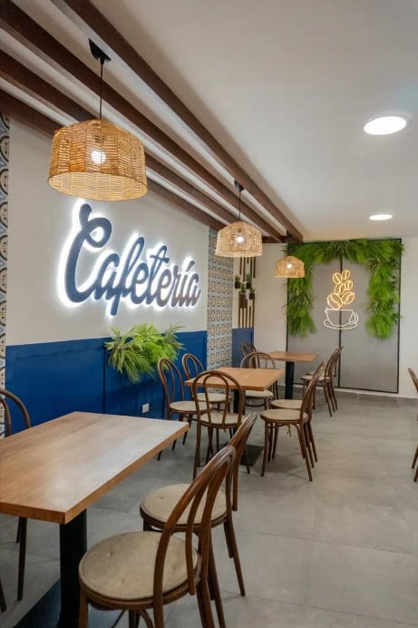 Modern cafe interior with blue neon Cafeteria sign, wooden chairs, pendant lamps, and green plant wall decor