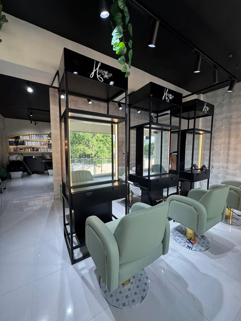 Modern salon interior with individual black-framed styling stations, green client chairs, and minimalist design with green plant accents overhead