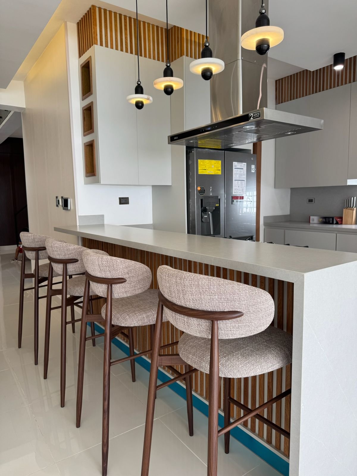 Modern kitchen with white island, three bar stools, pendant lights, and wood paneling accents