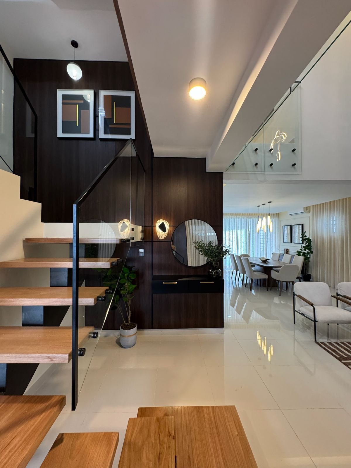 Modern interior with dark wooden loft staircase, open-concept living space, white marble flooring, and contemporary furniture