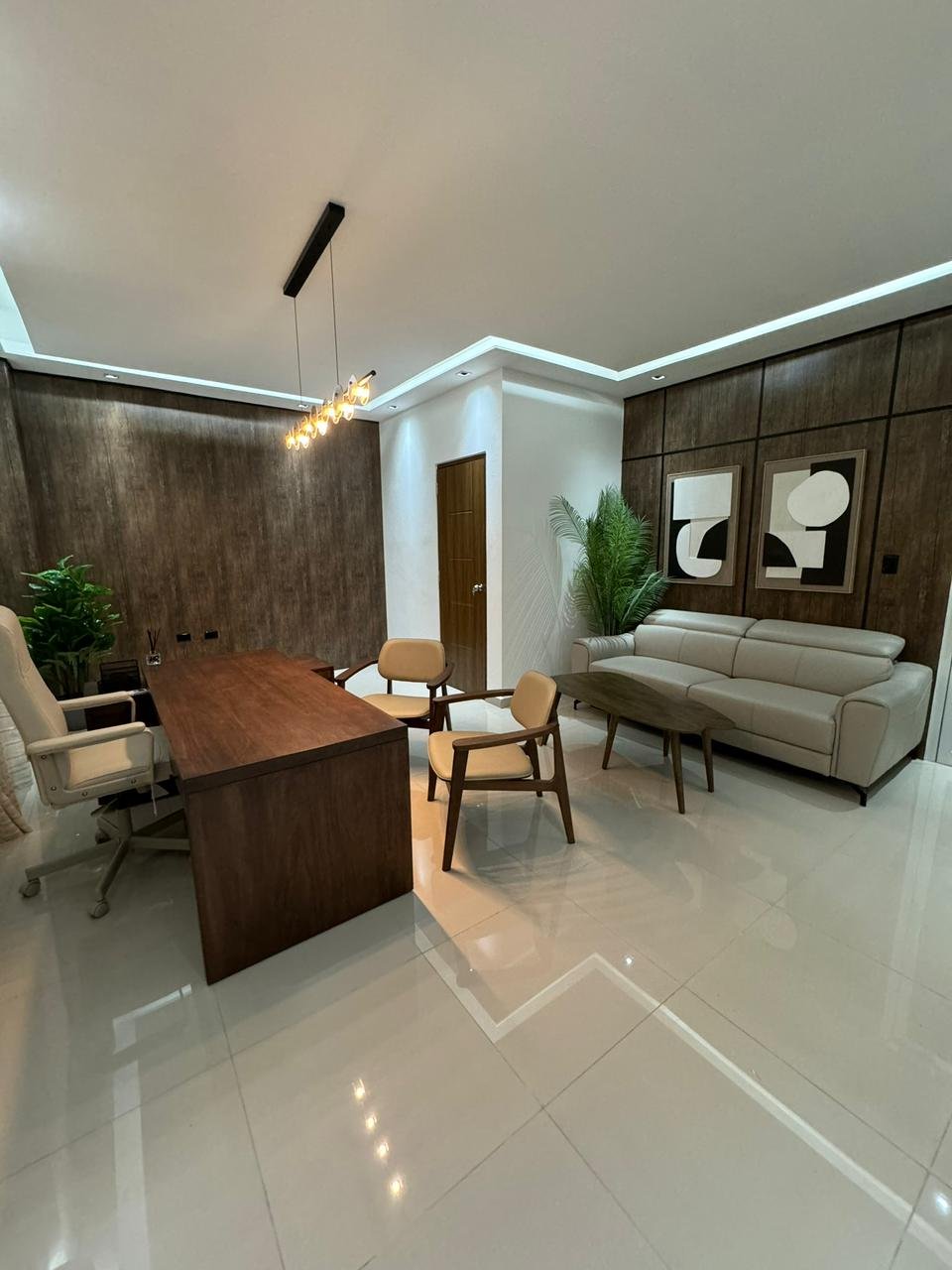 Modern office interior with dark wood desk, beige sofa, decorative plants, contemporary lighting, and polished white floors