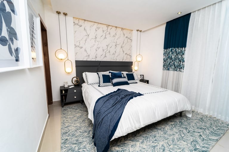 Modern bedroom with king bed, navy and white bedding, marble headboard, pendant lights, dark nightstands, and white curtains